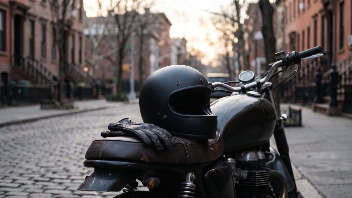 A black full-face motorcycle helmet and gloves resting on the seat of a parked motorcycle in morning light