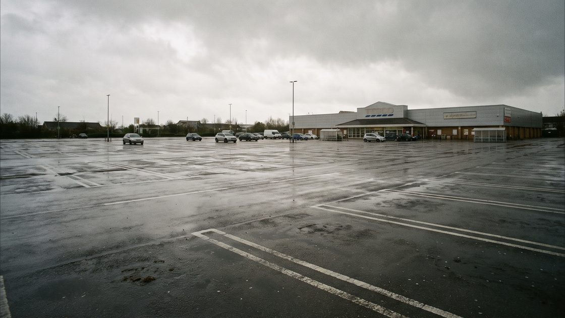 A large, mostly empty retail parking lot on a wet overcast day, with lane markings on the wet asphalt