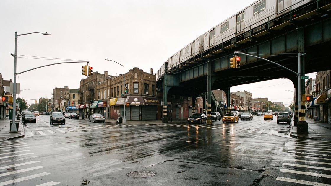 A Queens street corner after rain, with elevated subway tracks overhead