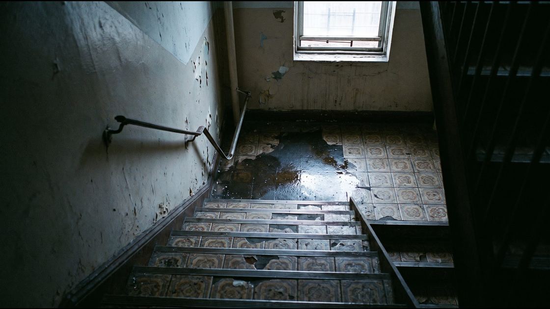 A worn tiled stairwell in an older New York building with a wet patch on the steps